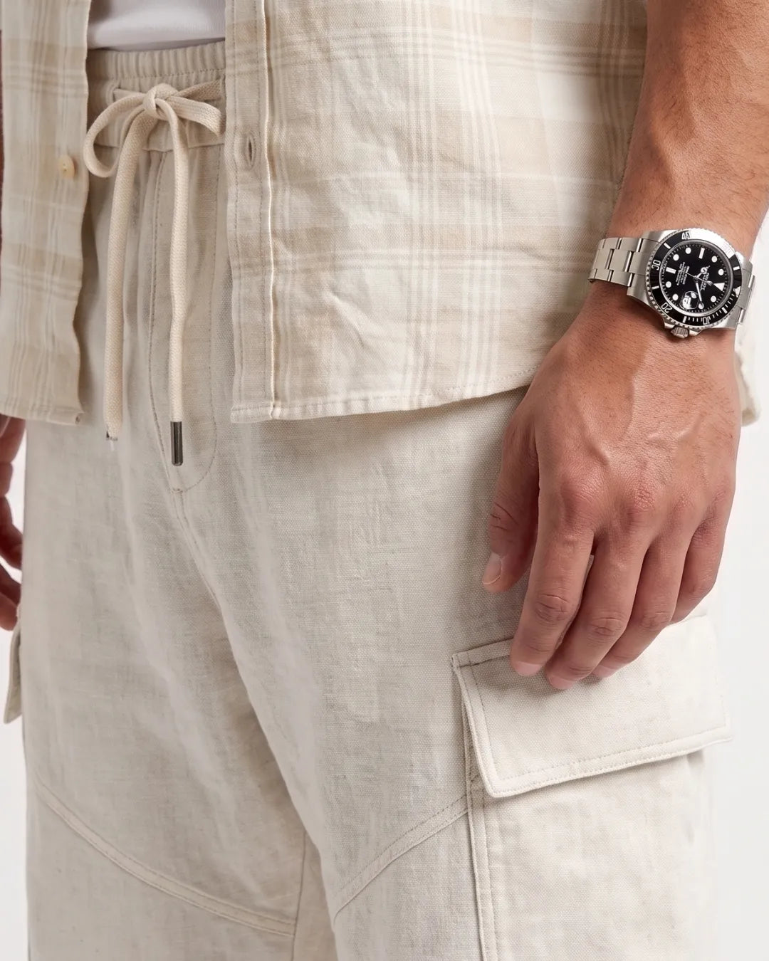 Close-up of a person wearing light beige linen cargo shorts with a side pocket and drawstring waist, paired with a matching plaid shirt and a silver wristwatch.