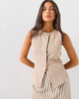 Front view of a woman wearing ONLY beige brown sleeveless waistcoat top with metallic buttons and striped trousers against a plain background
