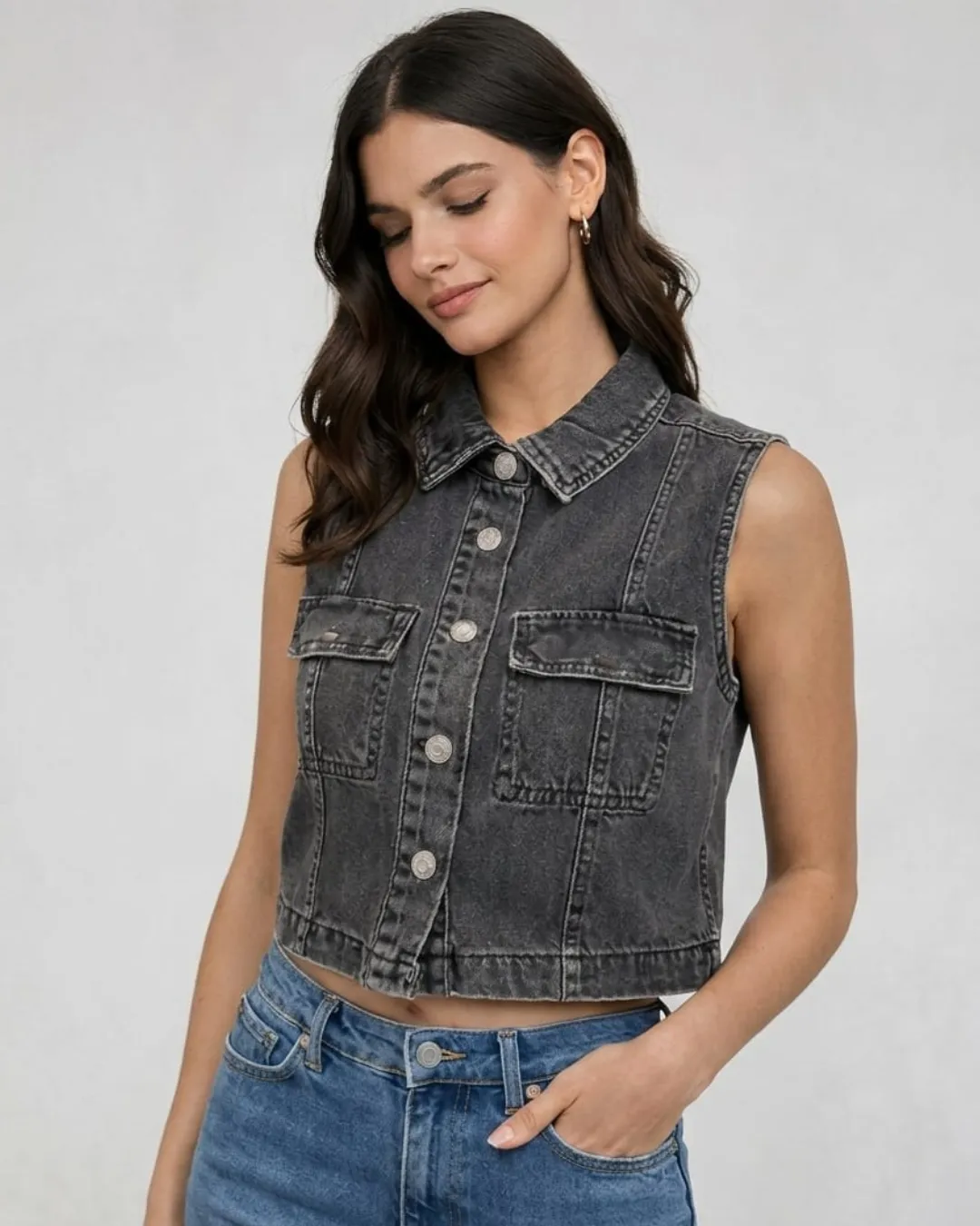 Faded black sleeveless denim jacket with cropped fit and button front design. A bold and modern piece that adds effortless style to everyday outfits.